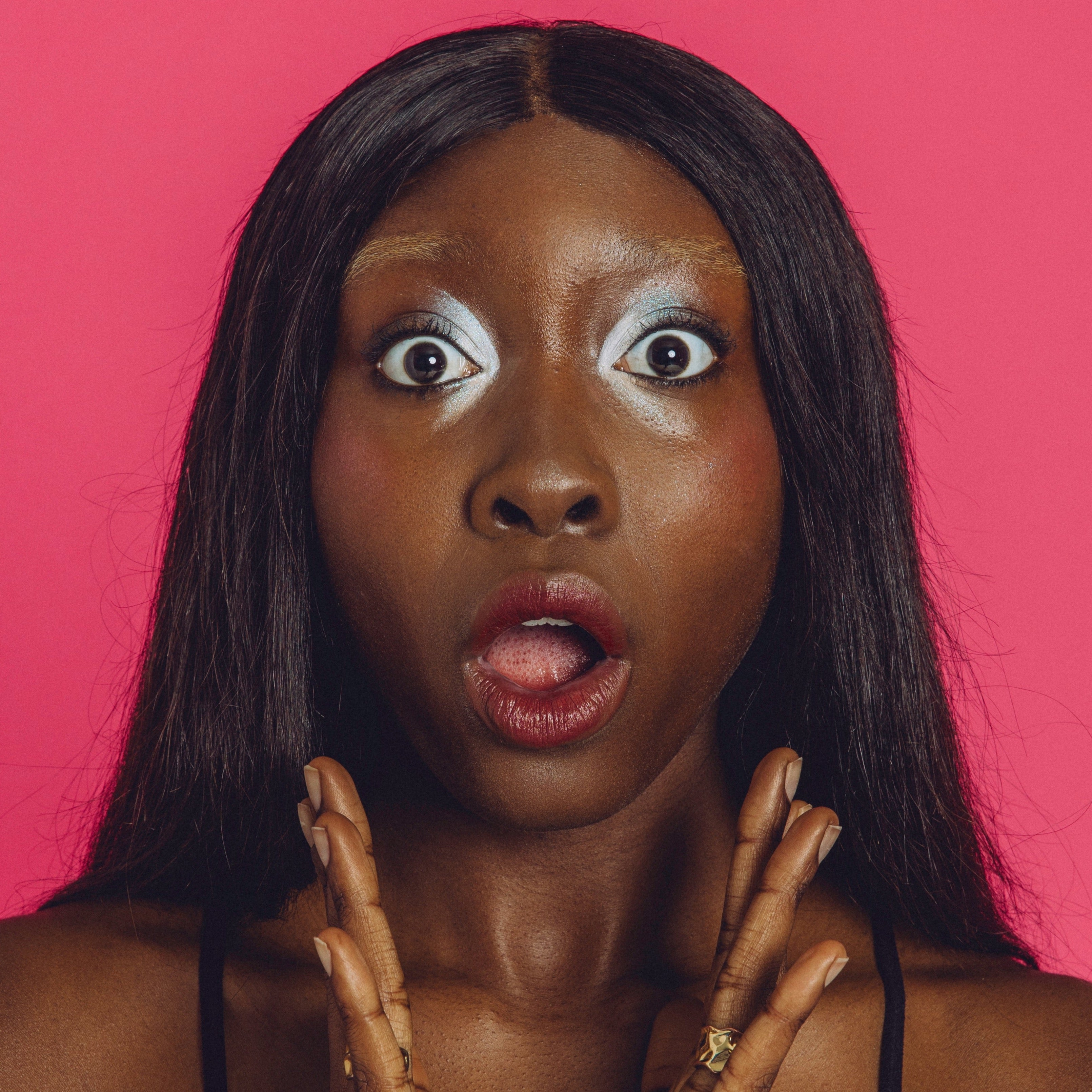 Black woman wearing a shimmery silver and blue eyeshadow look does a shocked face.