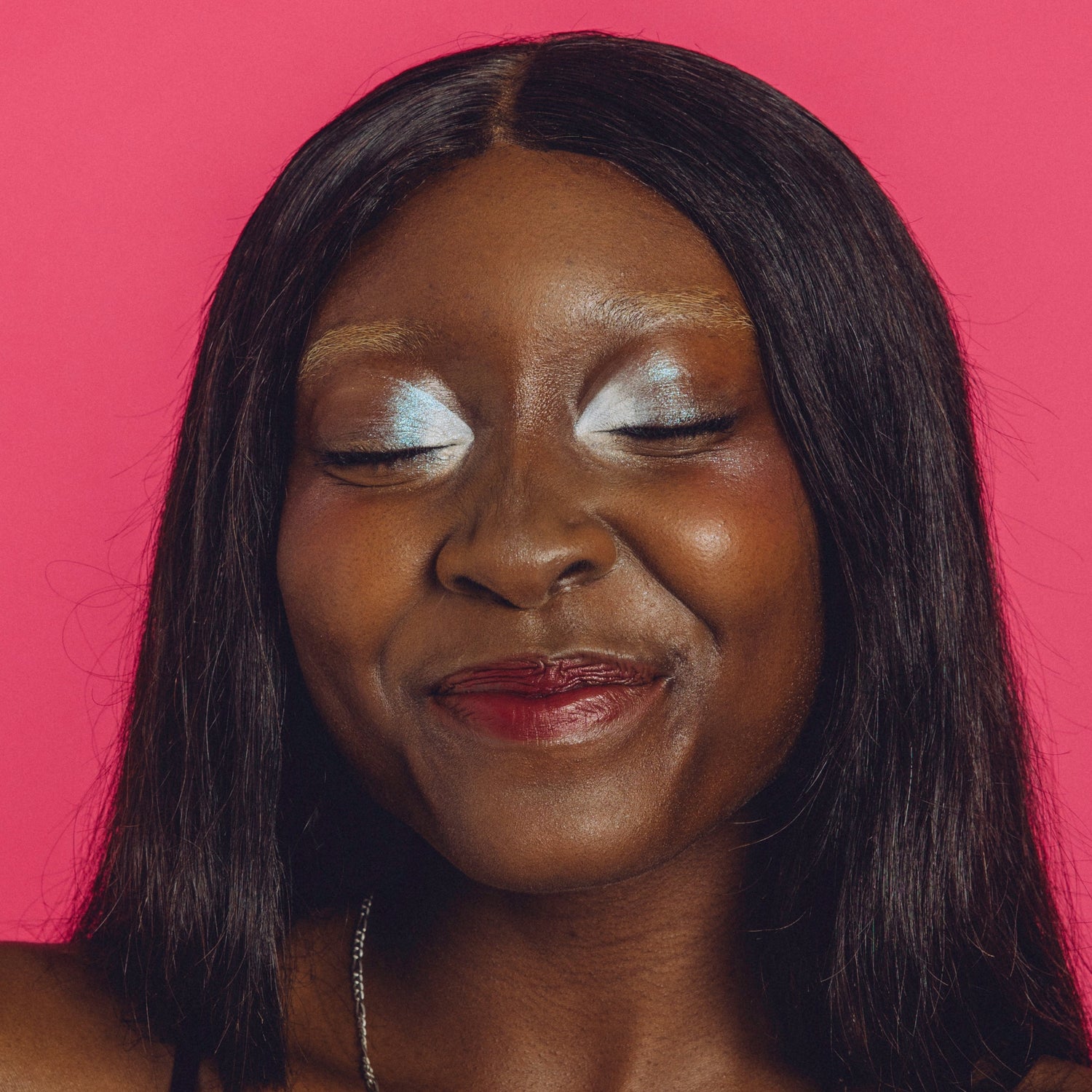 Woman with shimmery silver eyemakeup smiles with her eyes closed.