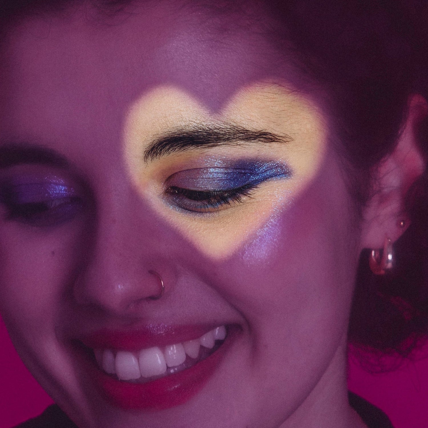 Woman smiling with heart shadow, showcasing her shimmery blue and purple eyemakeup.