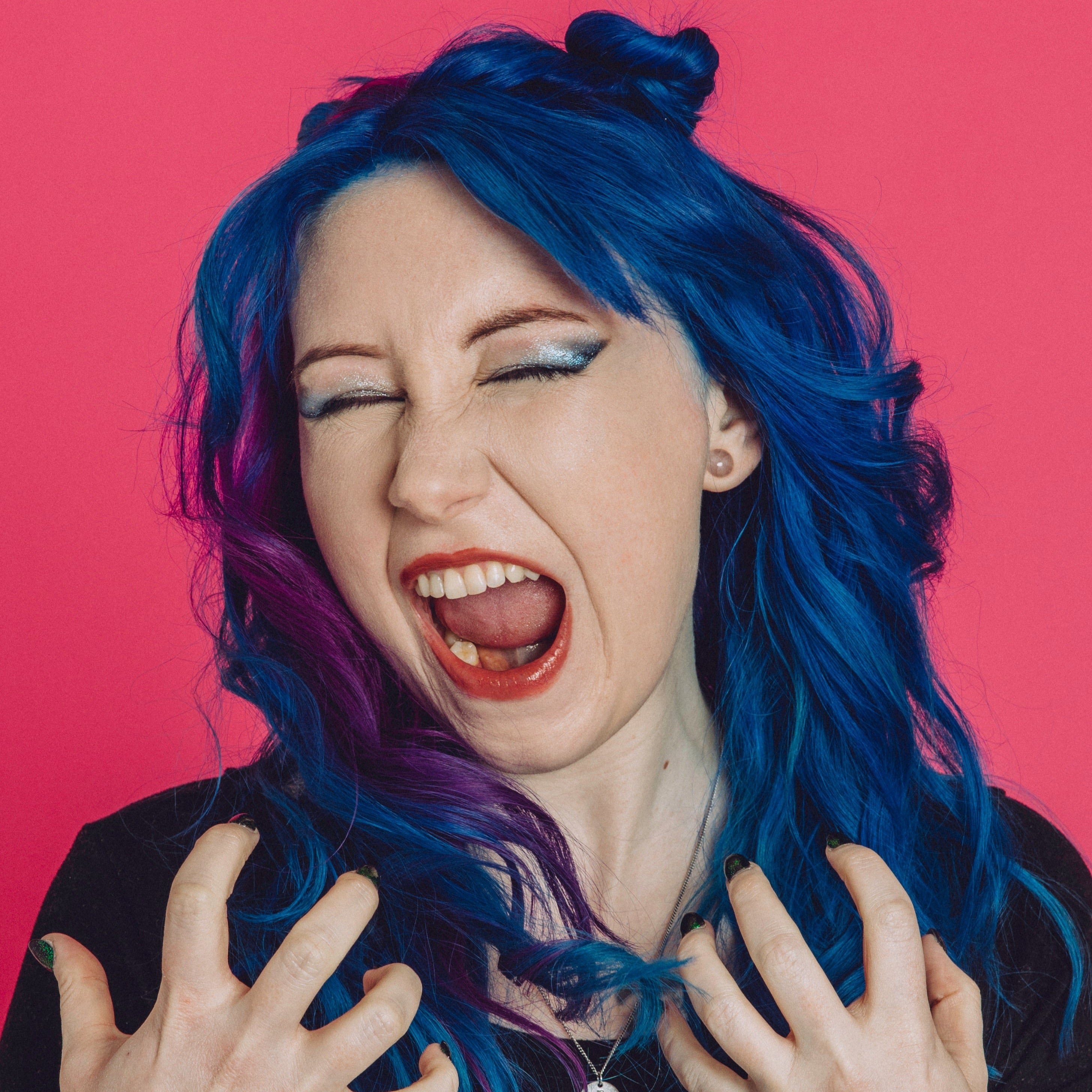 White woman with dyed blue and purple hair wears a shimmery blue eyeshadow look and screams.