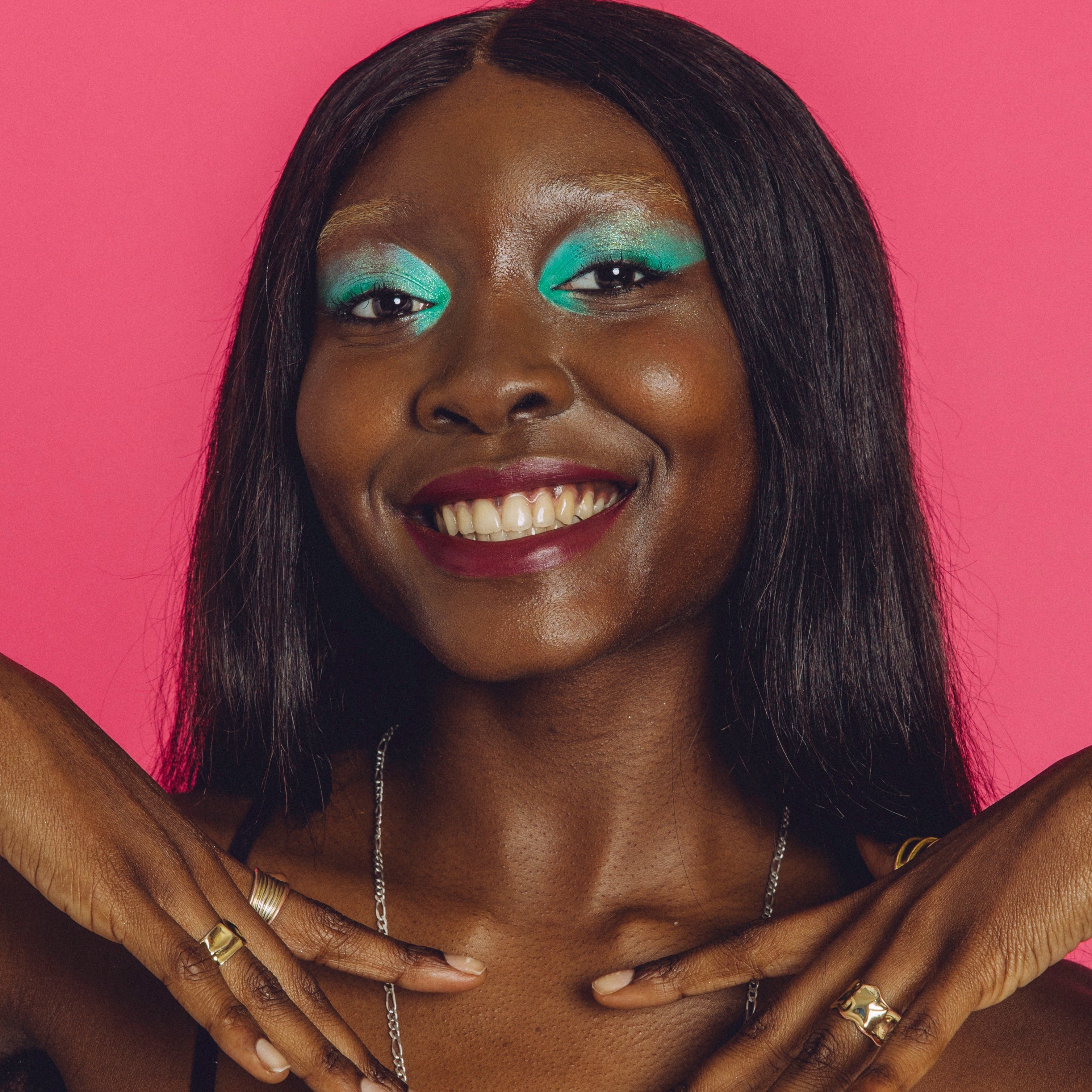 Black woman wearing a shimmery silver and green eyeshadow look smiles.