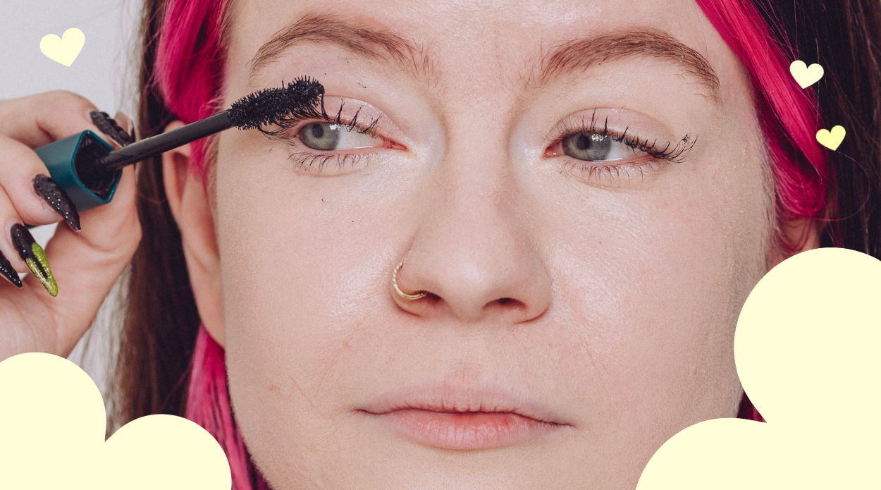 A close up image of just Millie Clare's eyes. She has the Human Beauty Liquid Confidence Mascara in her hand. She has pink eyebrows and hair,and blue eyes