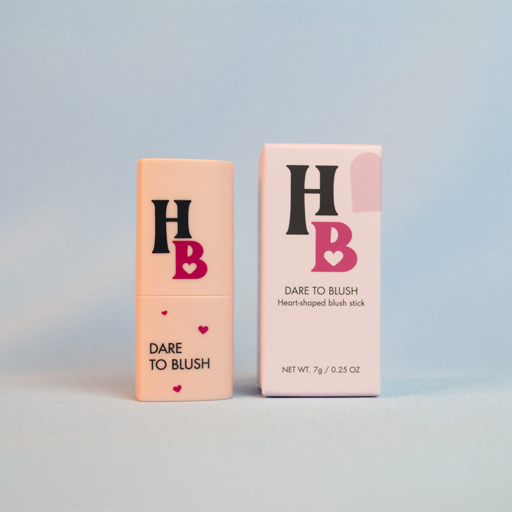 the Dare To Blush heart-shaped blush stick next to the box in front of a blue background
