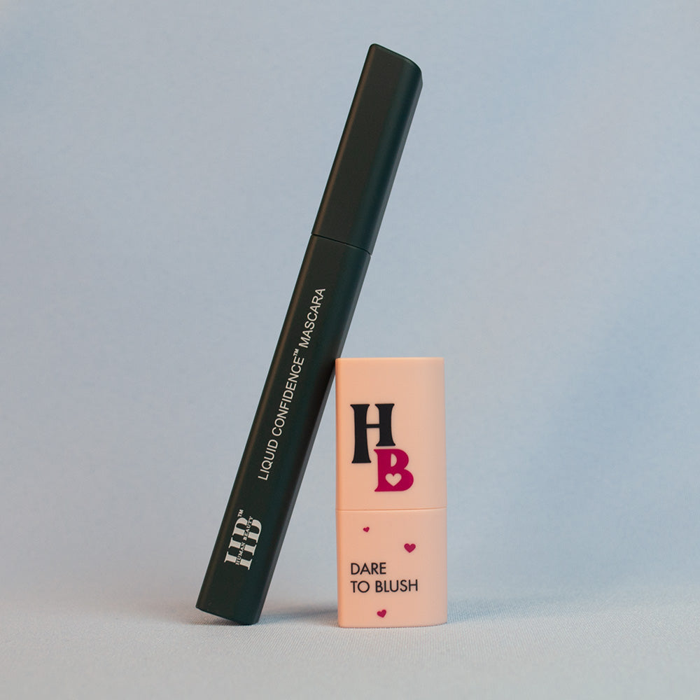 A Liquid Confidence mascara and a Dare To Blush heart-shaped blush stick in front of a light blue background