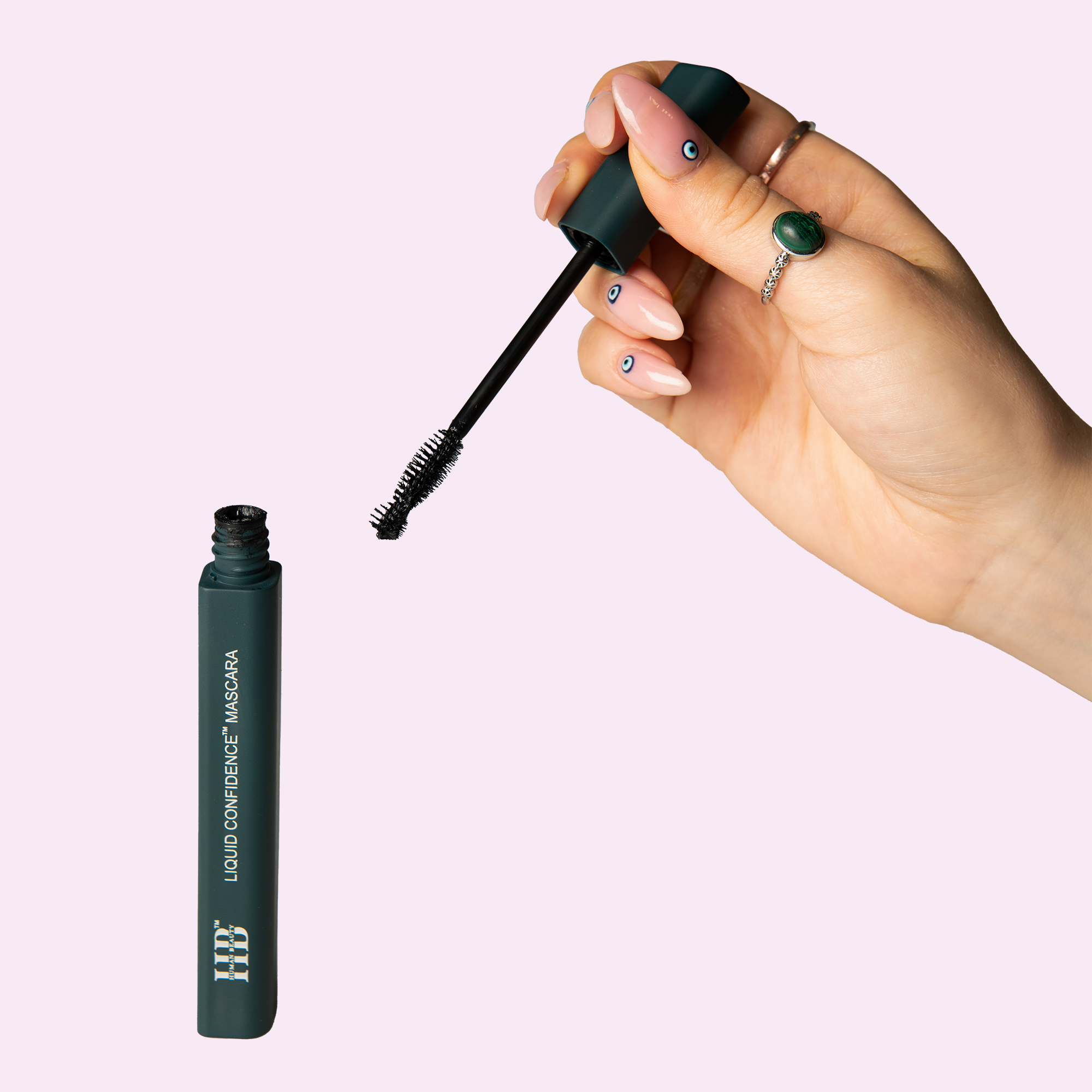 The Liquid Confidence Mascara held open by a hand on a light purple background