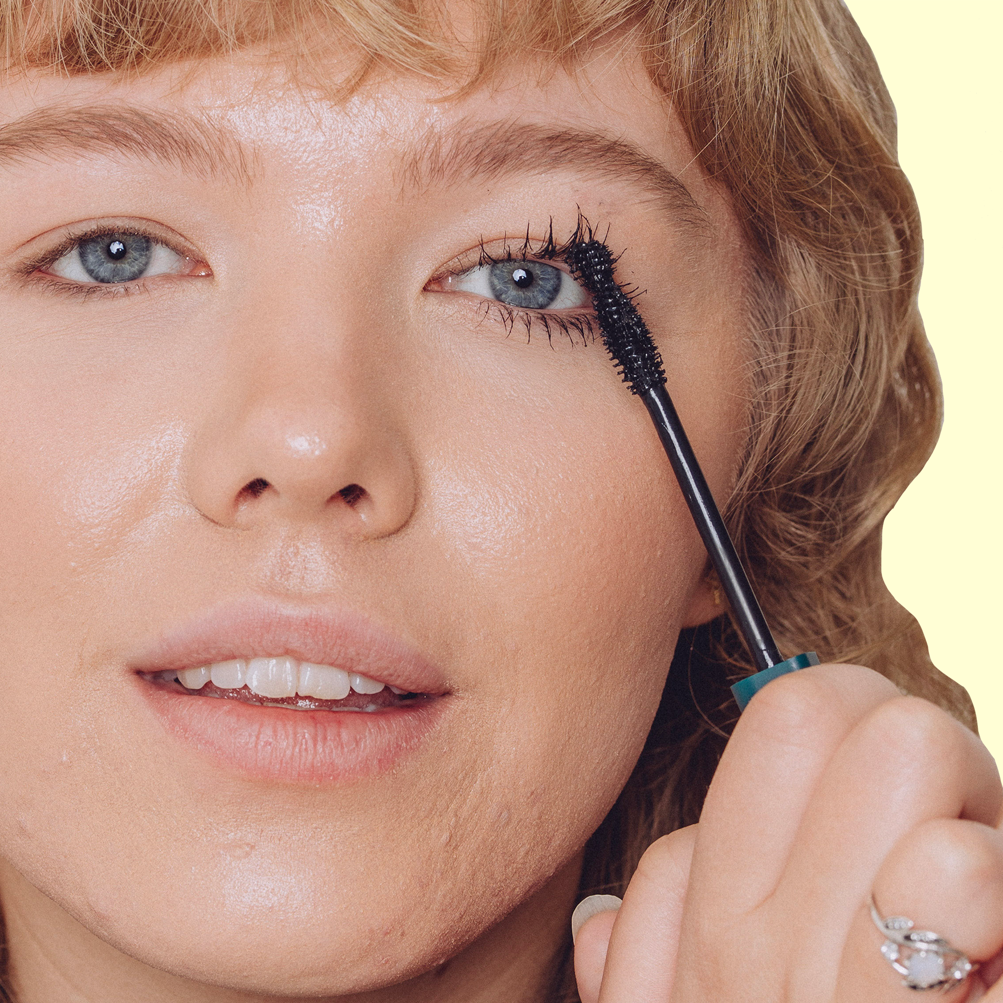 A girl with grip mobility issues using The Liquid Confidence Mascara vertically on a light yellow background