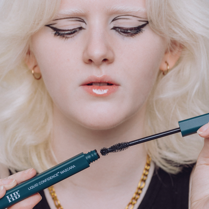 A girl with white hair and fair features opening The Liquid Confidence Mascara.