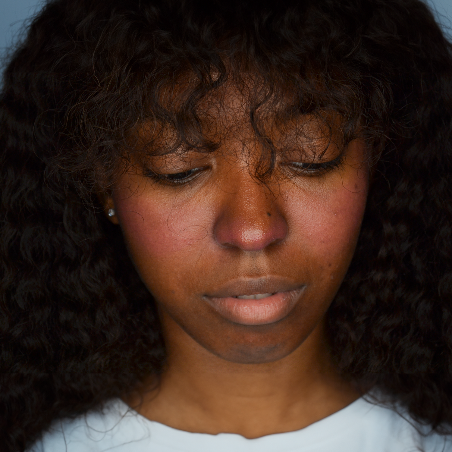 Close up picture of a model wearing the Dare To Blush heart-shaped blush stick in shade Bold Berry on her cheeks. She has dark skin and curly dark hair