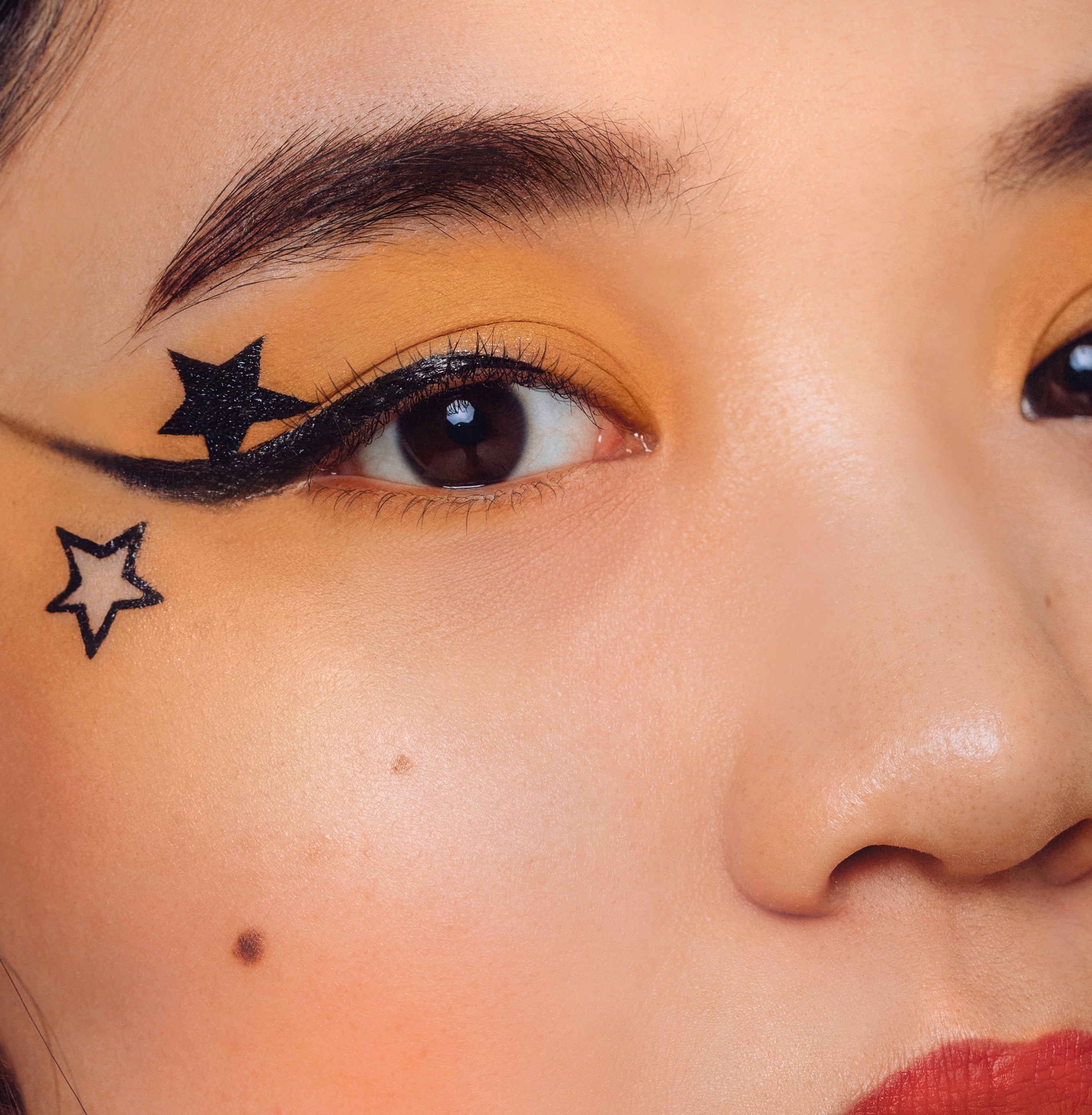A orange matte eye makeup look using shade Armour from the Makeup Therapy Palette. with a bold black eyeliner and black stars.