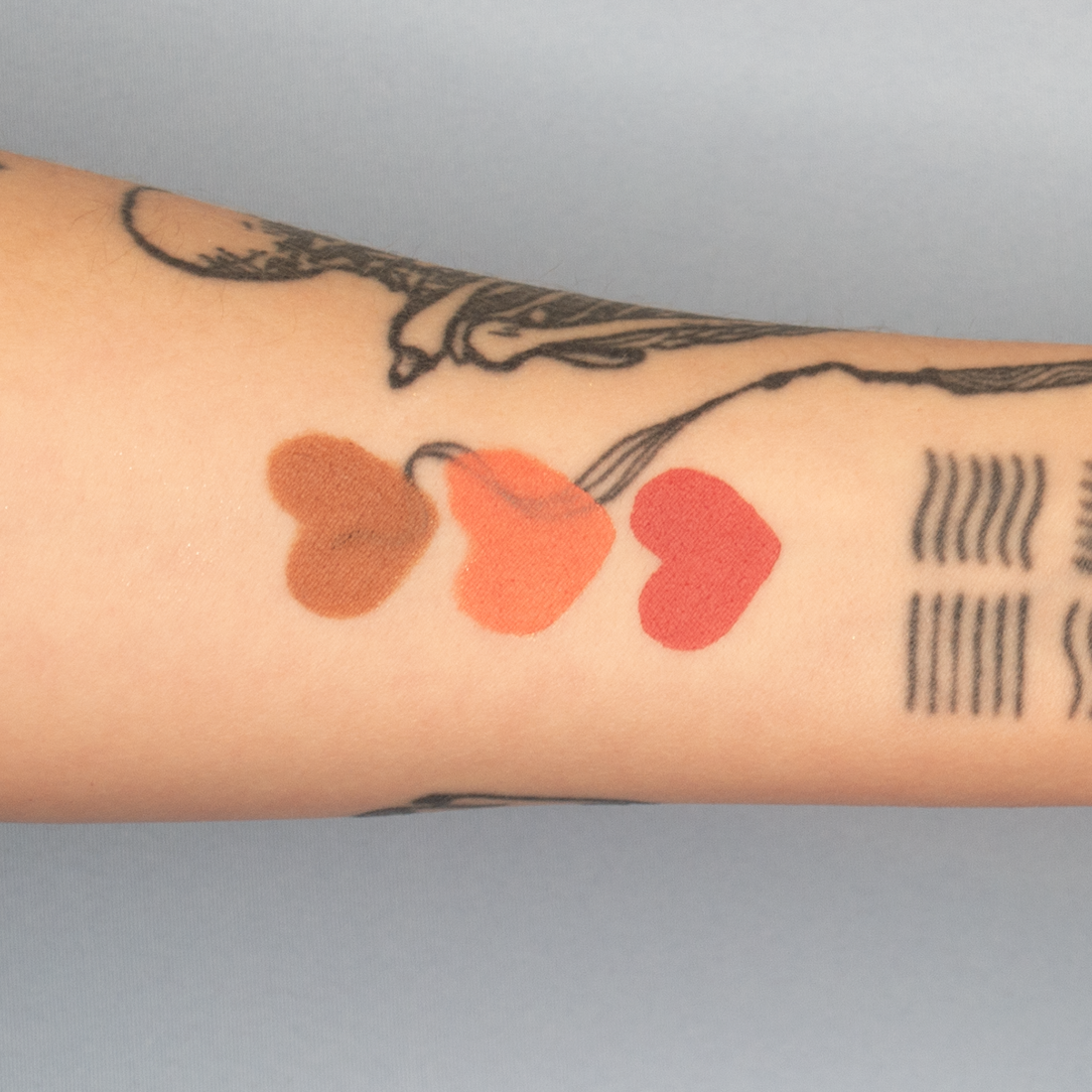 Swatch of colors Confident Coral, Brilliant Bronze and Restful Rose in heart shape on tattooed fair skin